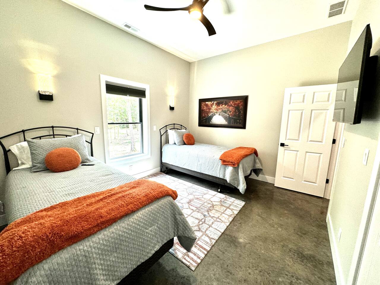 Wall sconces and a large ceiling fan provide ample lighting. This bedroom has two windows to view large trees lots outside.