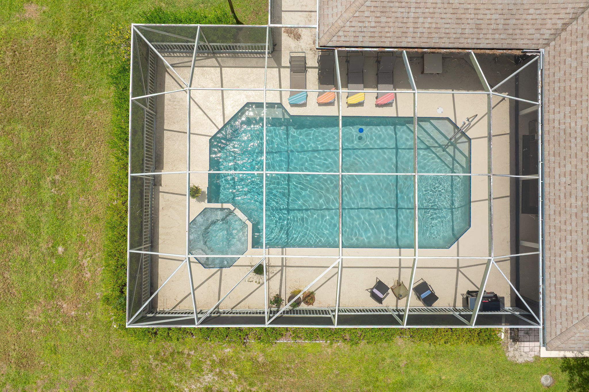 Screened-in pool and spa with ample deck space, loungers, and grill, ideal for relaxing or entertaining outdoors.