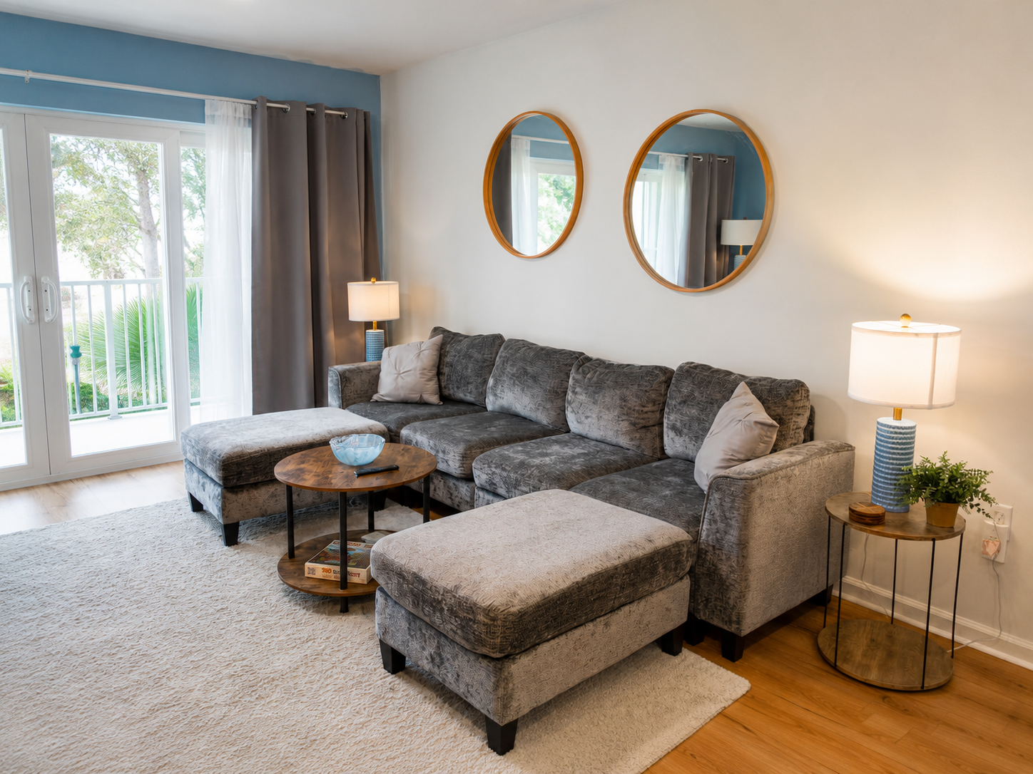 Modern living room with gray sectional, round mirrors, and bright natural light.
