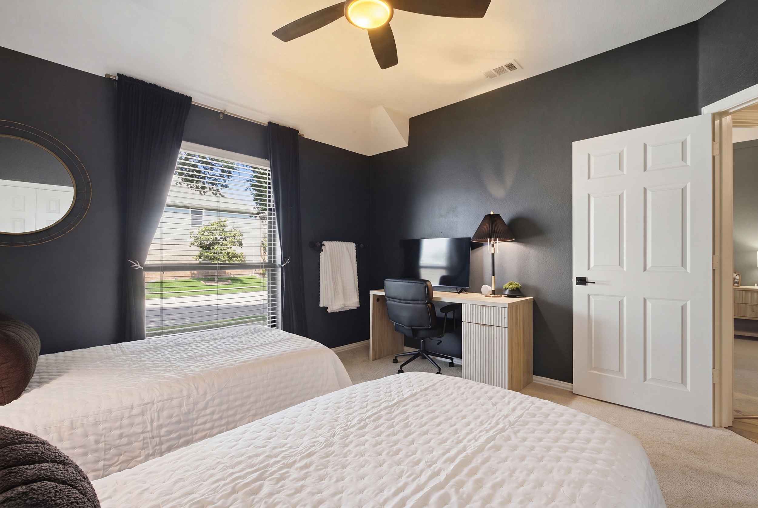 Guest Bedroom 3 with a dedicated workspace including a desk and office chair, plus a 55-inch Smart TV. Bright window keeps the space airy and inviting.
