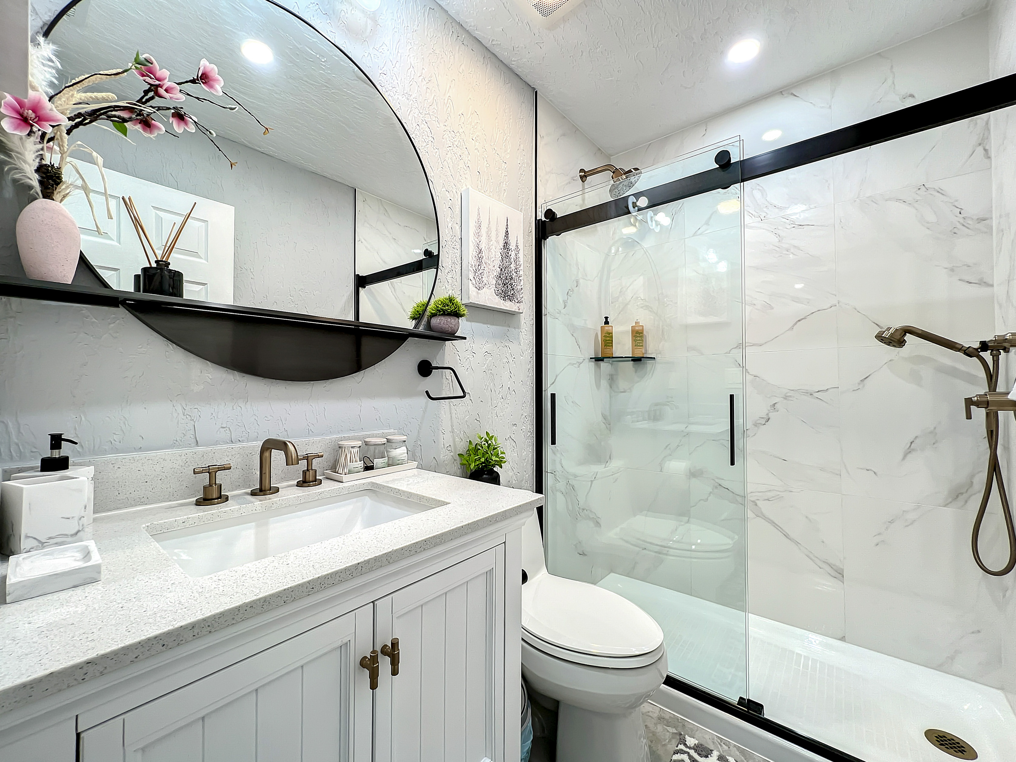 Elegant bathroom featuring a large circular mirror, double vanity, and spacious glass-enclosed shower with marble tile.