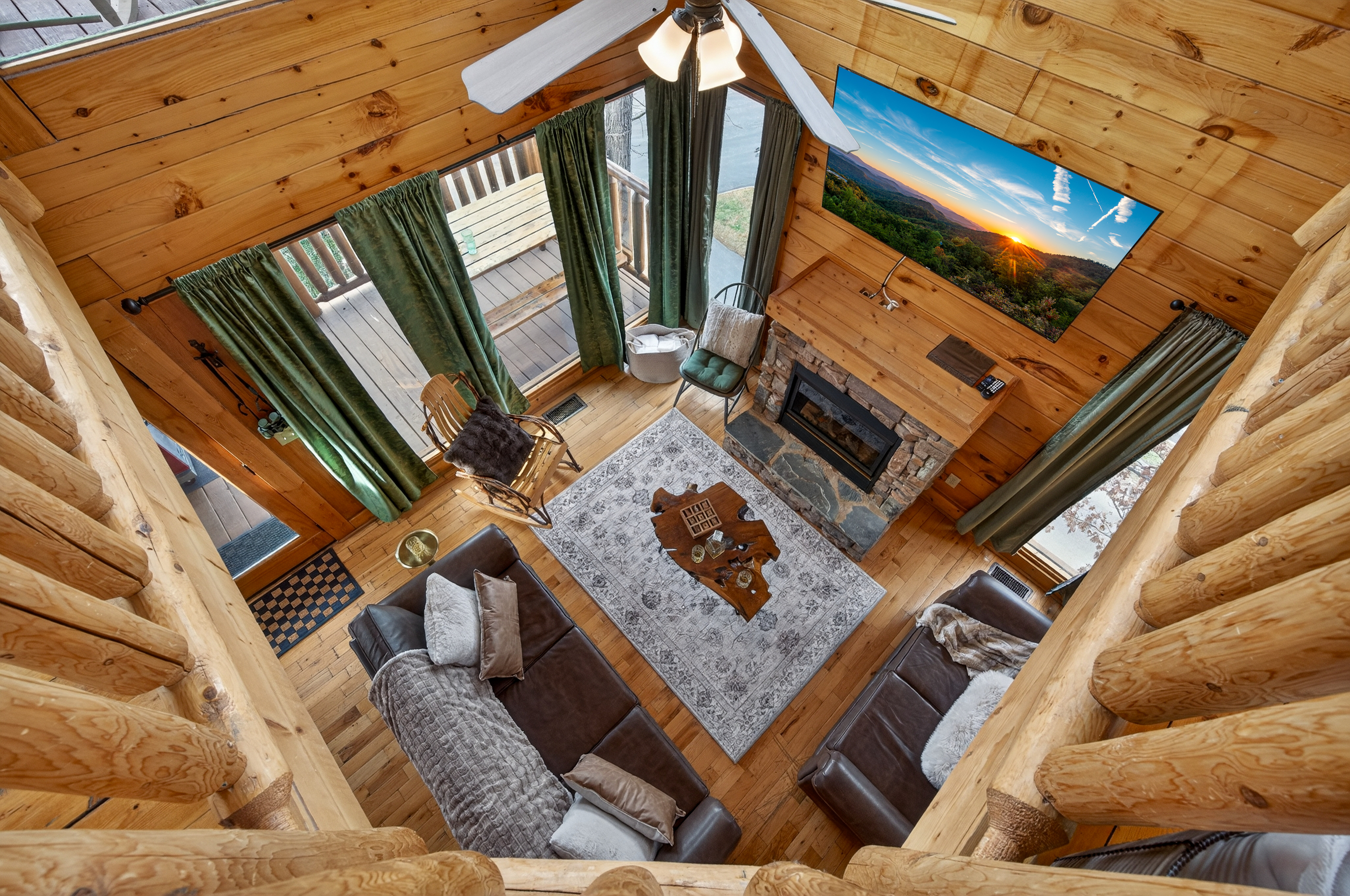 The view from the upper loft looking down — stone fireplace, leather sectional, deck access, and enough room for the whole group to spread out.