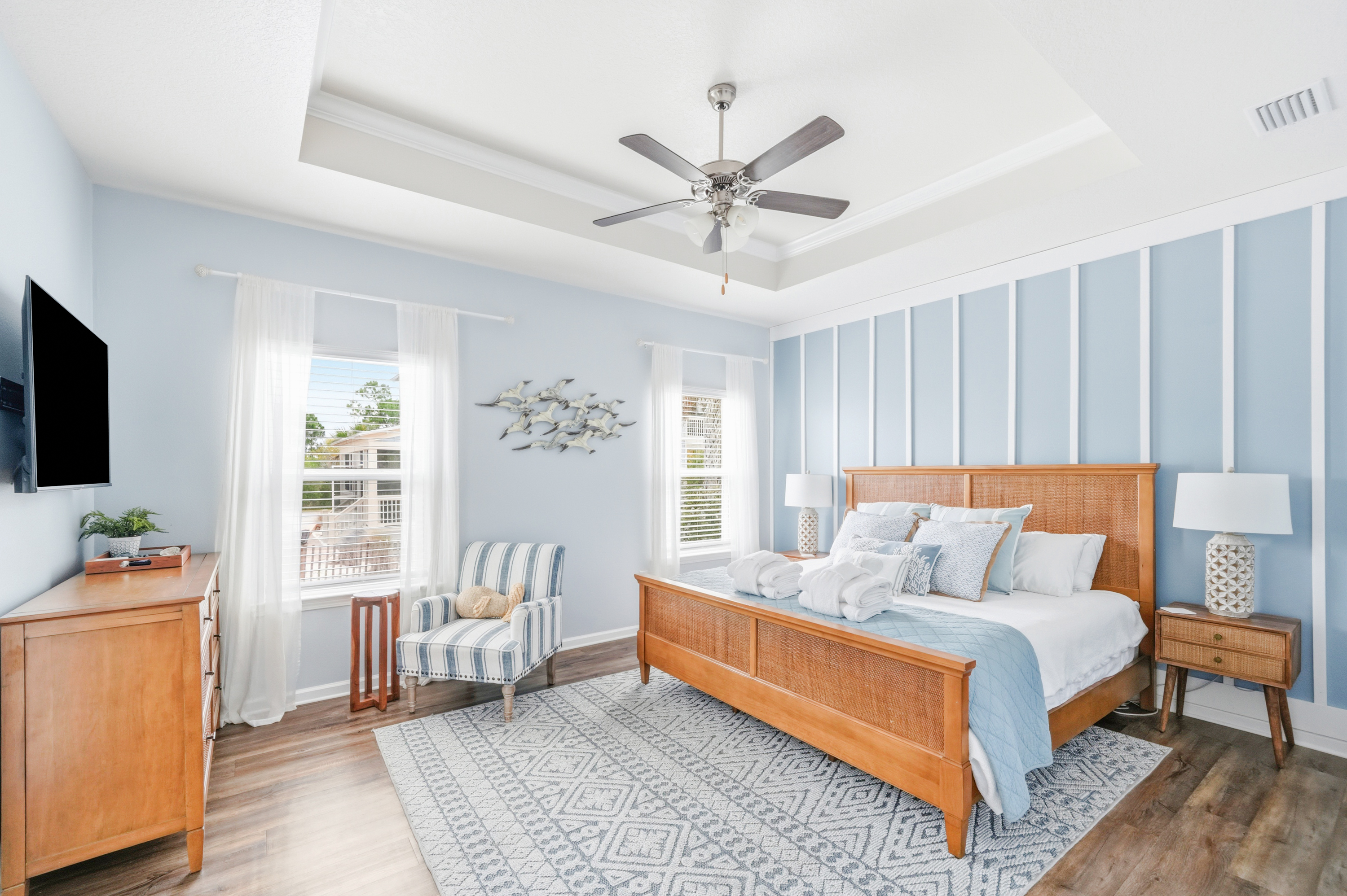 Primary Suite: Elegant King bedroom featuring an en suite bathroom, plush linens, ceiling fan, elegant bedside lamps, dresser, couch, and Smart TV.