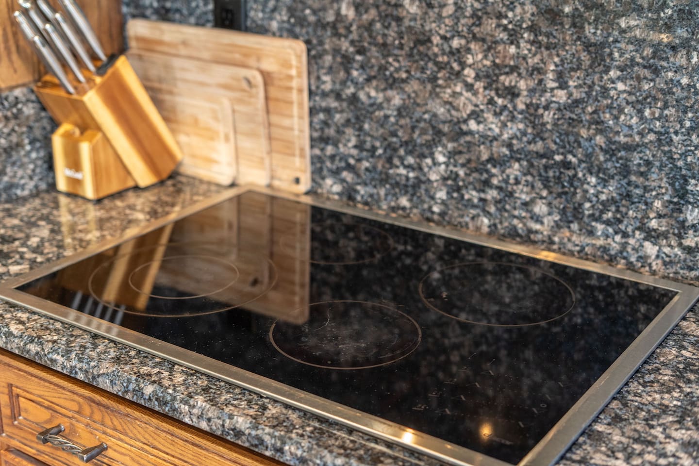 A sleek glass-top electric cooktop set into the granite counter, paired with a full knife set and cutting boards for the home chef.