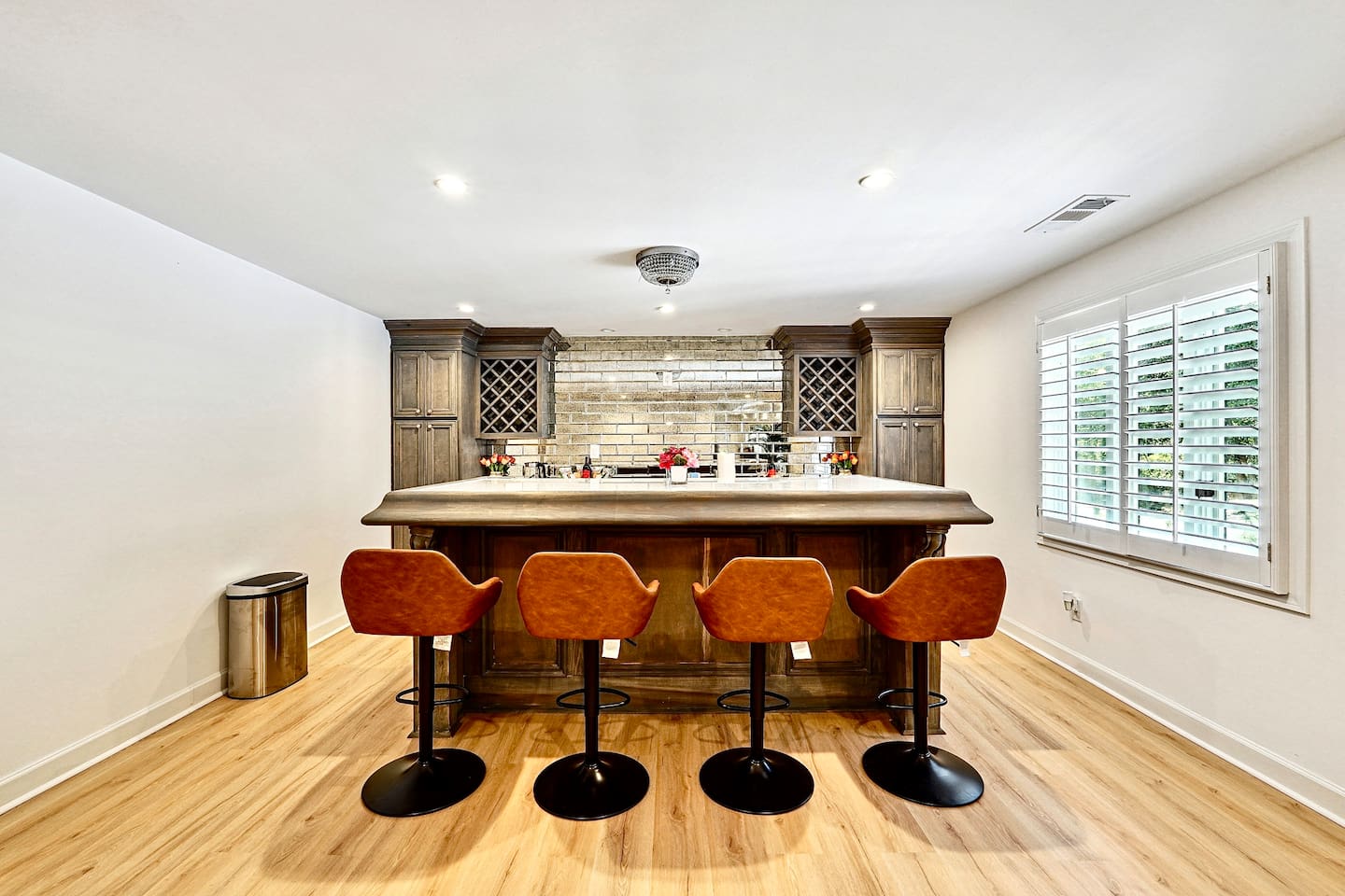 Basement kitchenette located to the left at the bottom of the stairs, featuring a sleek bar with seating, sink, two coolers, wine cabinetry, and modern gray cabinets with a matching backsplash, convenient as it is right next to the game room!

