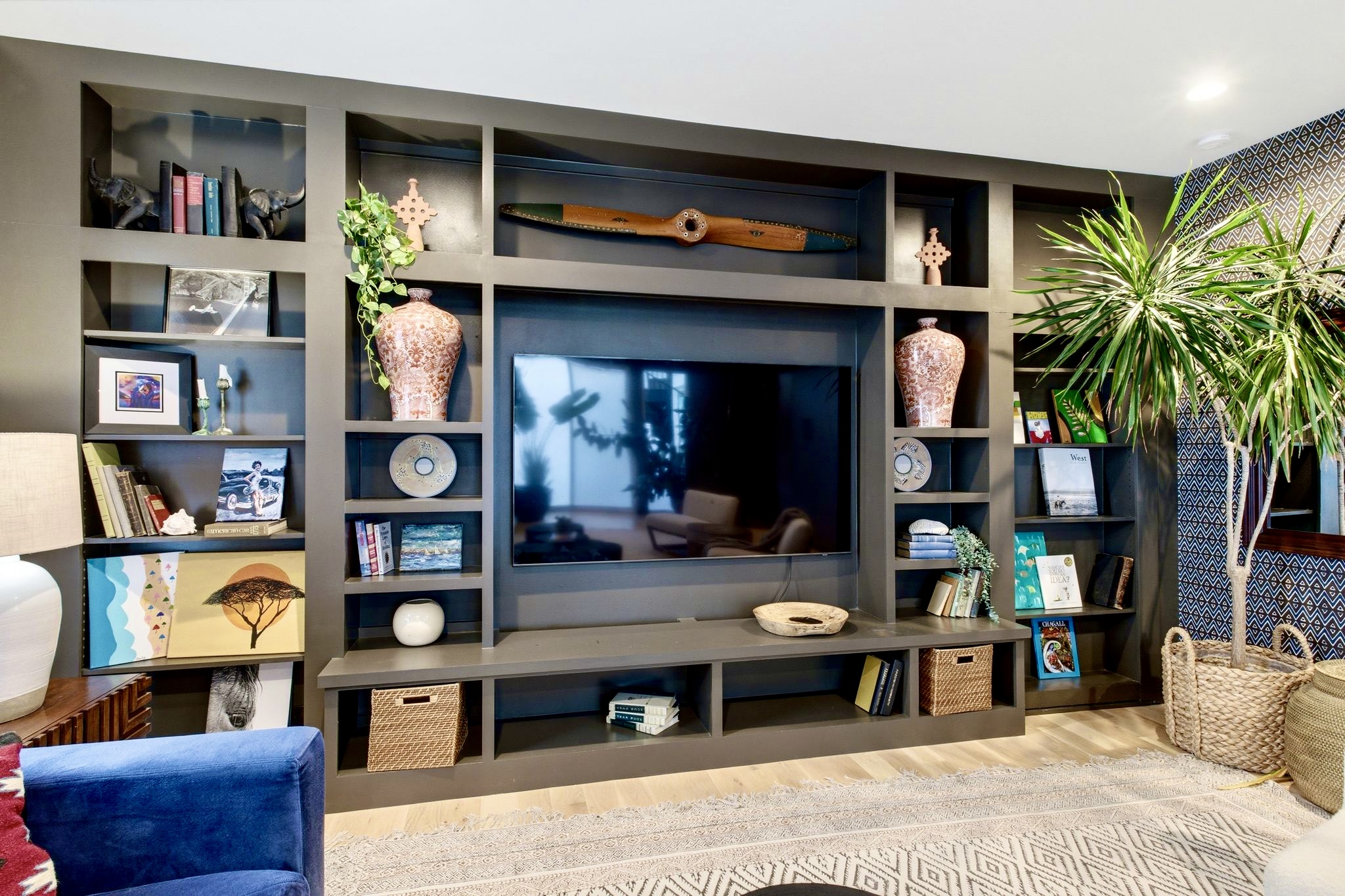 Built-in entertainment wall w/ shelving, TV & lush plants — stylish, functional & full of character.
