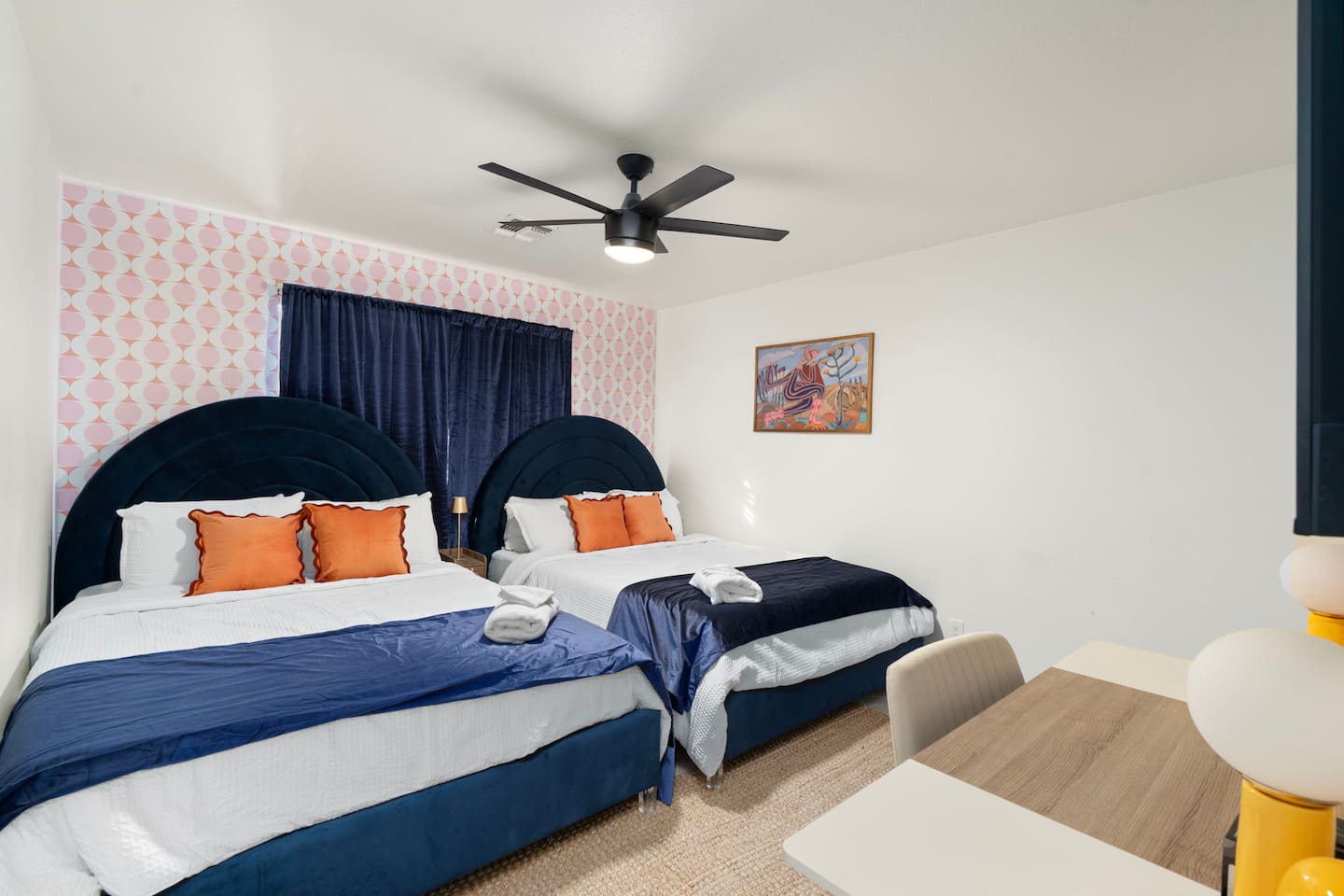 Guest bedroom with bold navy headboards, pink wallpaper accent, and orange pillows—a playful, modern space with personality.