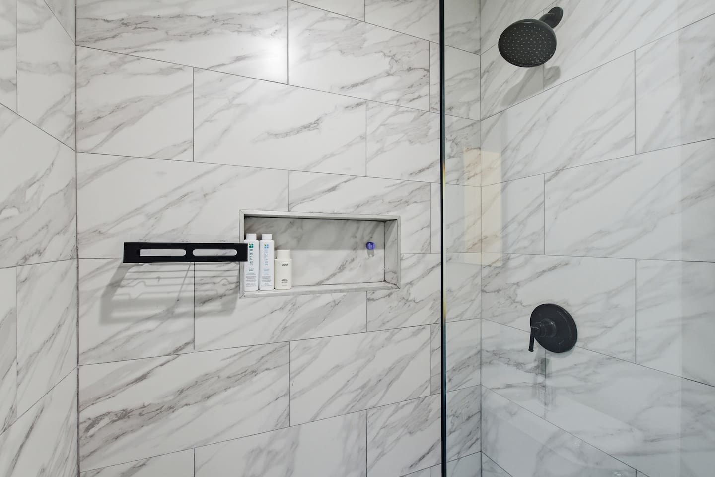 Spacious glass shower with rainfall-style head, built-in shelf, and elegant tile design.