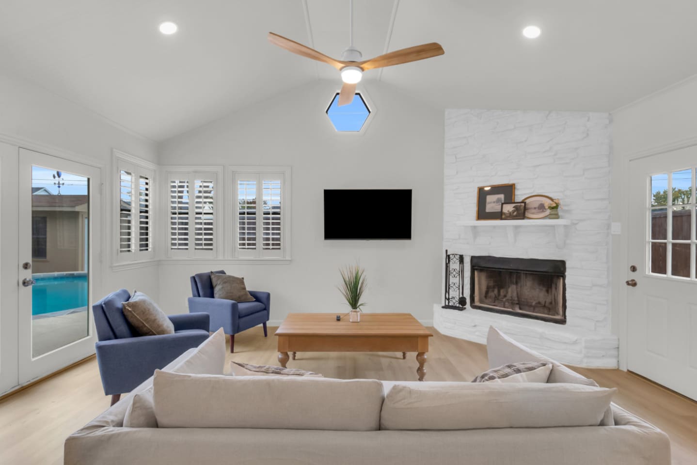Bright private living room with mounted TV, modern ceiling fan, and a charming indoor fireplace. Direct access to the pool through the private patio doors.