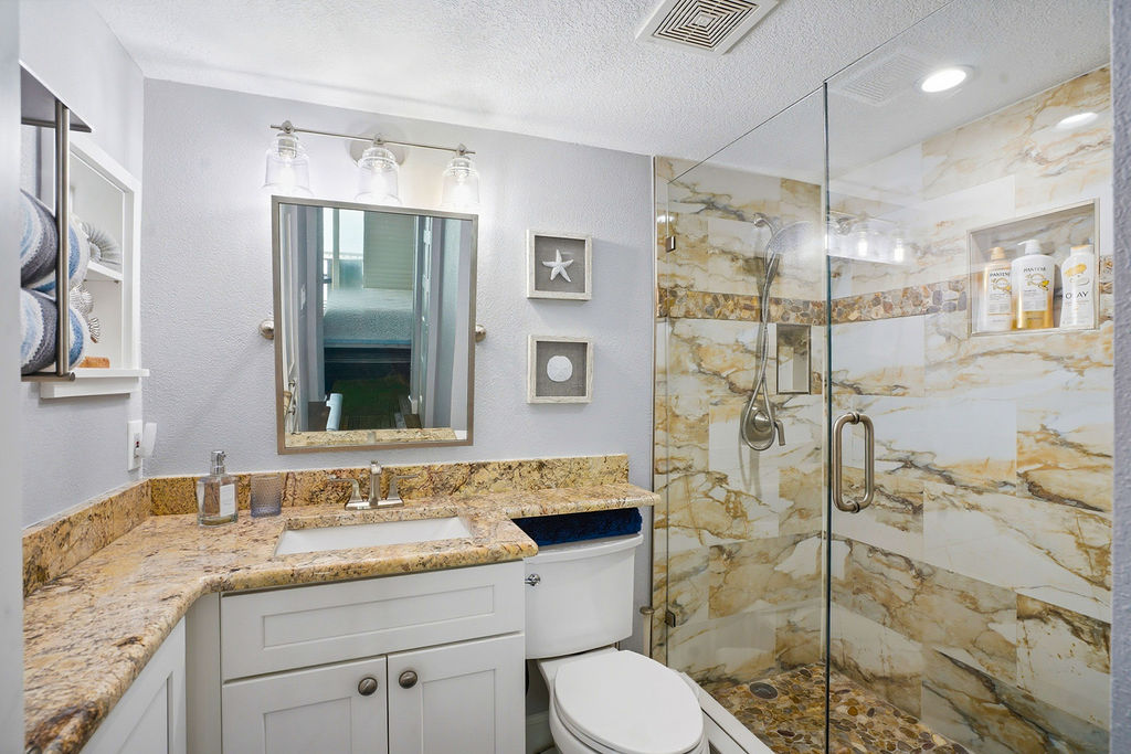 Updated spa-style bathroom featuring a glass walk-in shower with tile, granite vanity, premium bath amenities, and bright modern lighting.