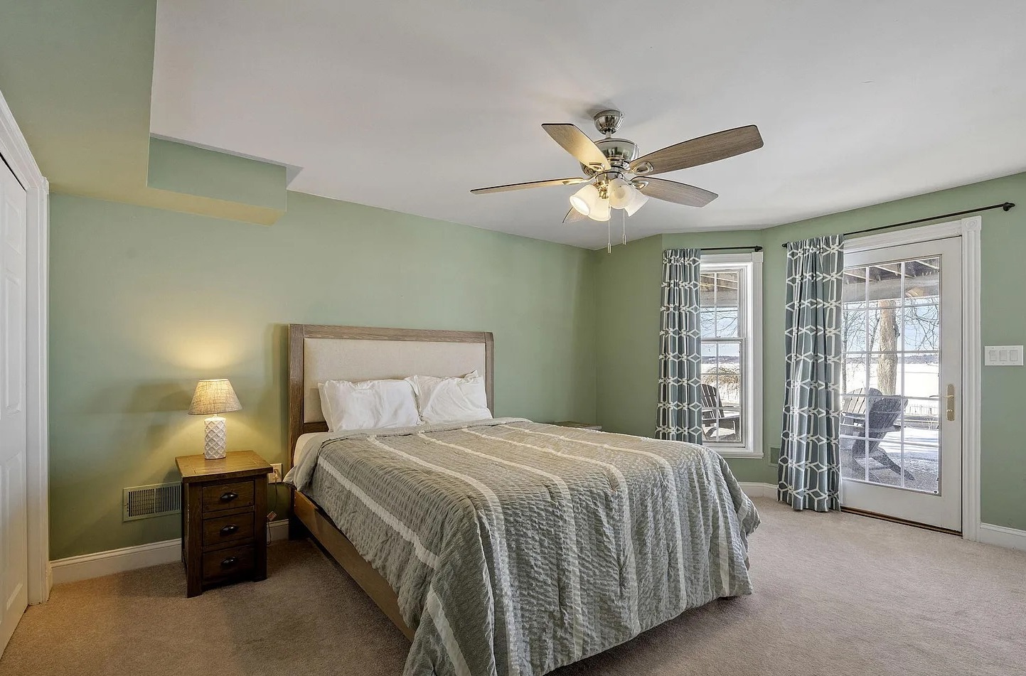 A peaceful ground-floor lakeview retreat with a queen bed, oversized windows overlooking the water, connected bathroom, TV ,desk+chair, and direct access to the outdoor patio and firepit area.