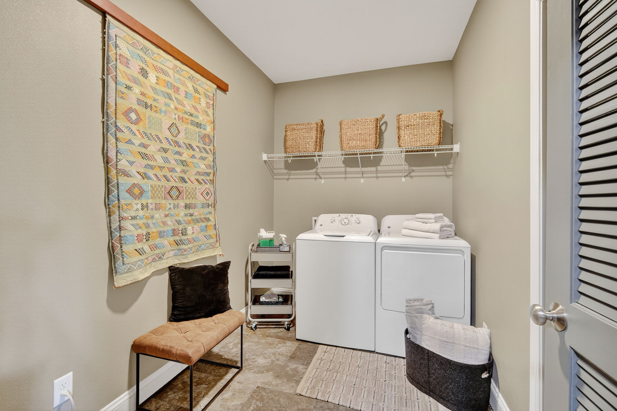 Convenience meets style in the oversized laundry room with washer, dryer, and open shelving. Thoughtful touches like a decorative wall hanging and bench seating elevate this space.