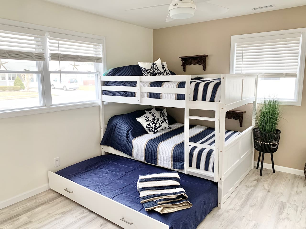 Perfect for kids or groups, this bright room features a white wooden bunk bed with nautical striped bedding and a pull-out trundle. Large windows fill the space with light, creating a cheerful spot for guests to rest.