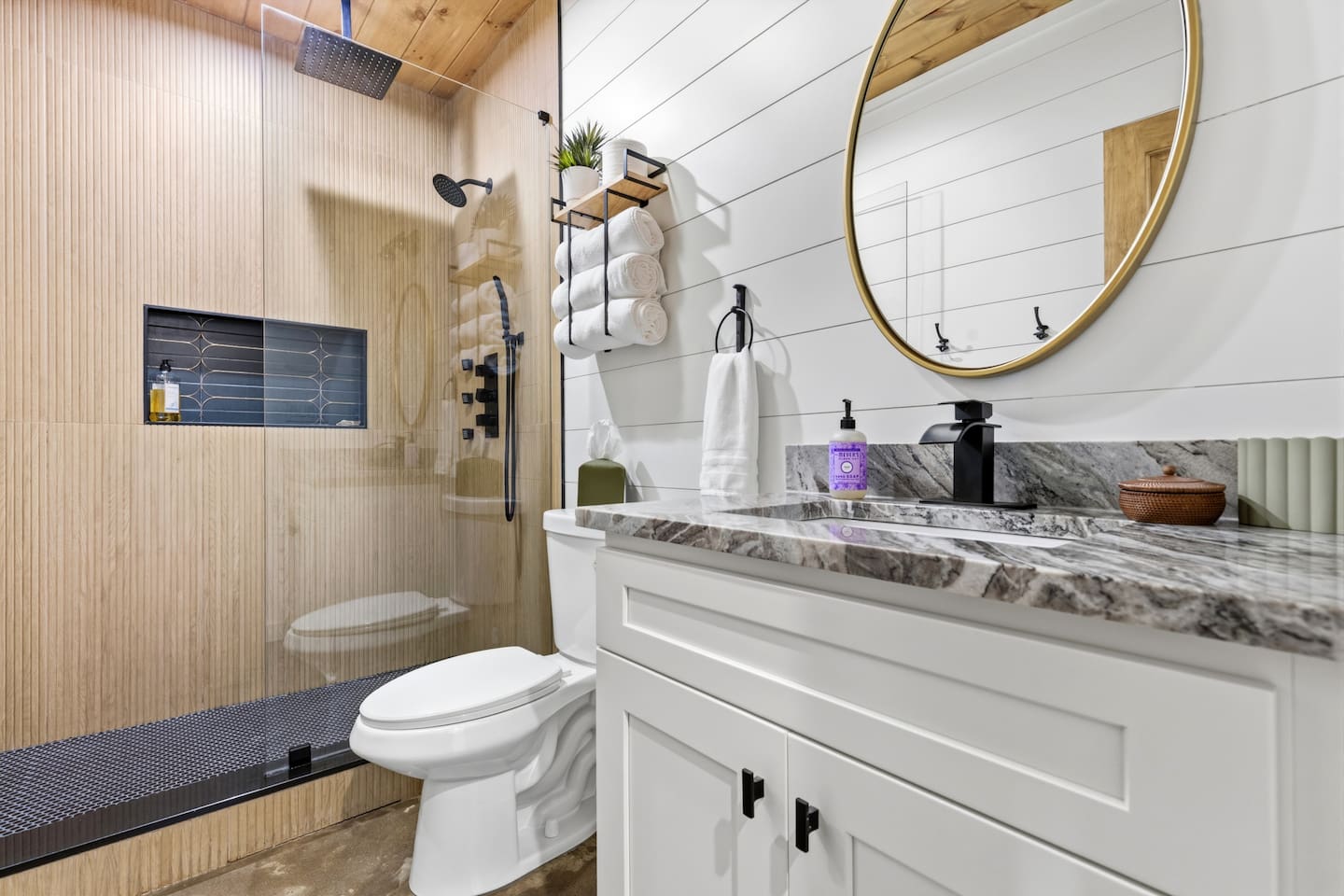 Luxury shower experience with a large rain shower head, standard shower head, three body jets, and a handheld sprayer. Sleek natural stone vanity and modern fixtures make this spa-like bathroom a highlight of the home.