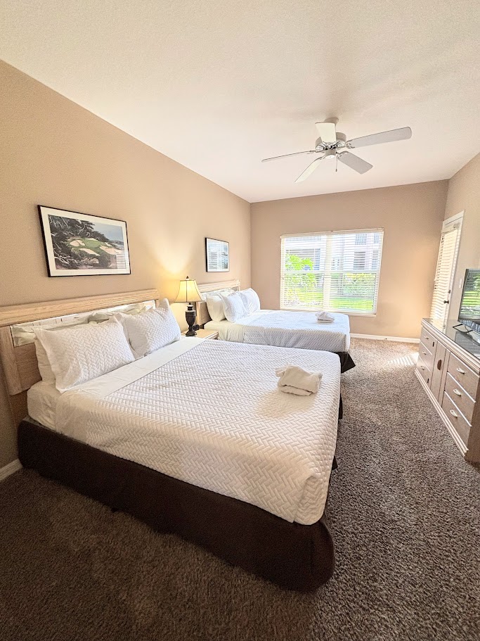 Spacious bedroom with two beds, dresser storage, ceiling fan, and a clean, relaxing setup.