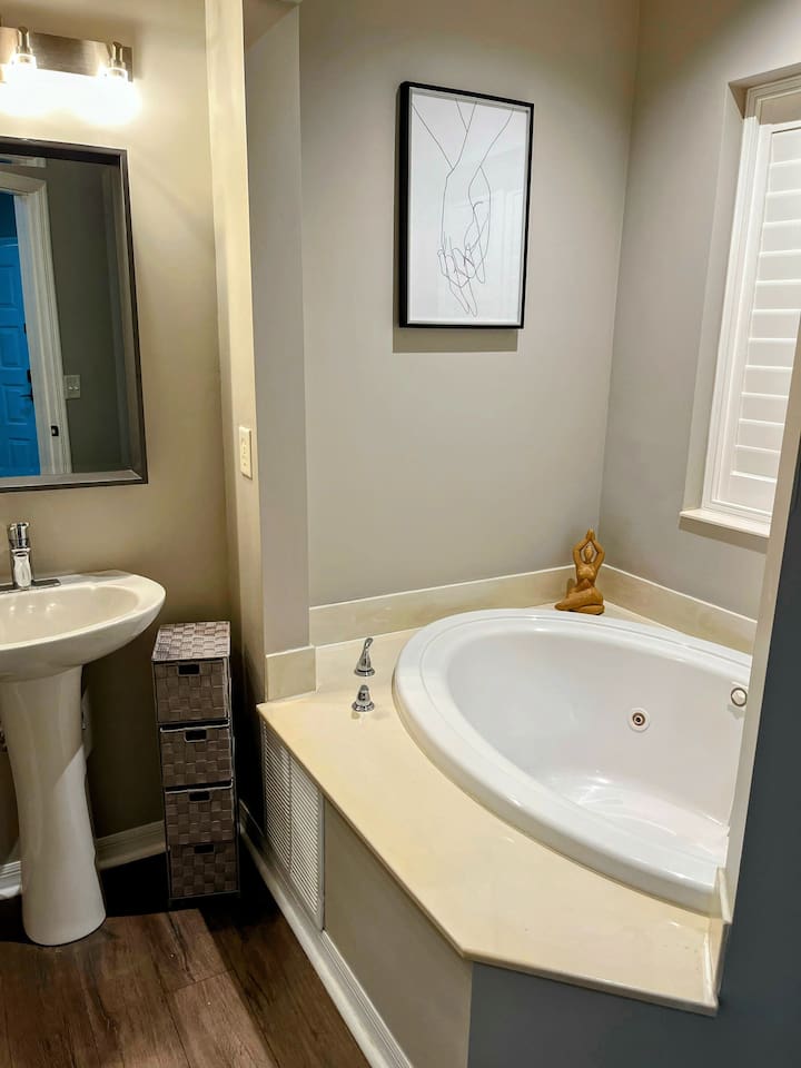 Bright bathroom with a soaking tub area, neutral finishes, and natural light from the window.