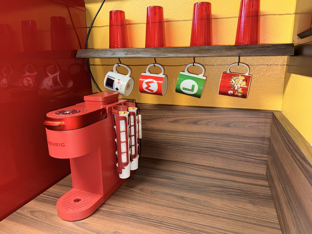 Convenient Keurig coffee maker at Mario's Mini Mansion in Clermont, FL! Mounted on the wall with colorful Mario-themed mugs (including power-up designs) hanging nearby—easy morning coffee for the whole family in our themed kitchen.