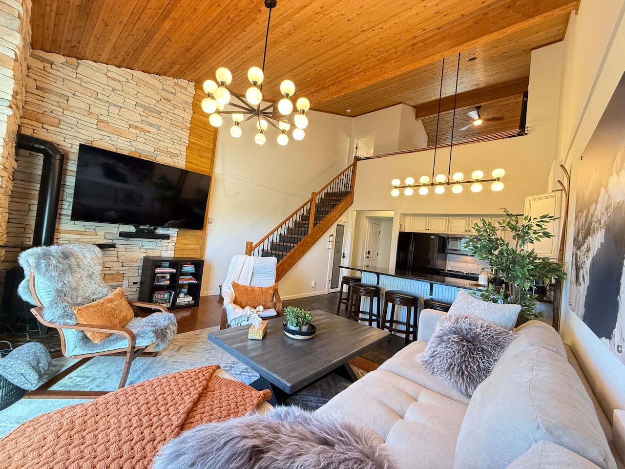 Bright open-concept living area with soaring cedar ceilings, a stone fireplace, and modern lodge lighting — the perfect place to unwind after exploring Kimberley’s mountain adventures.