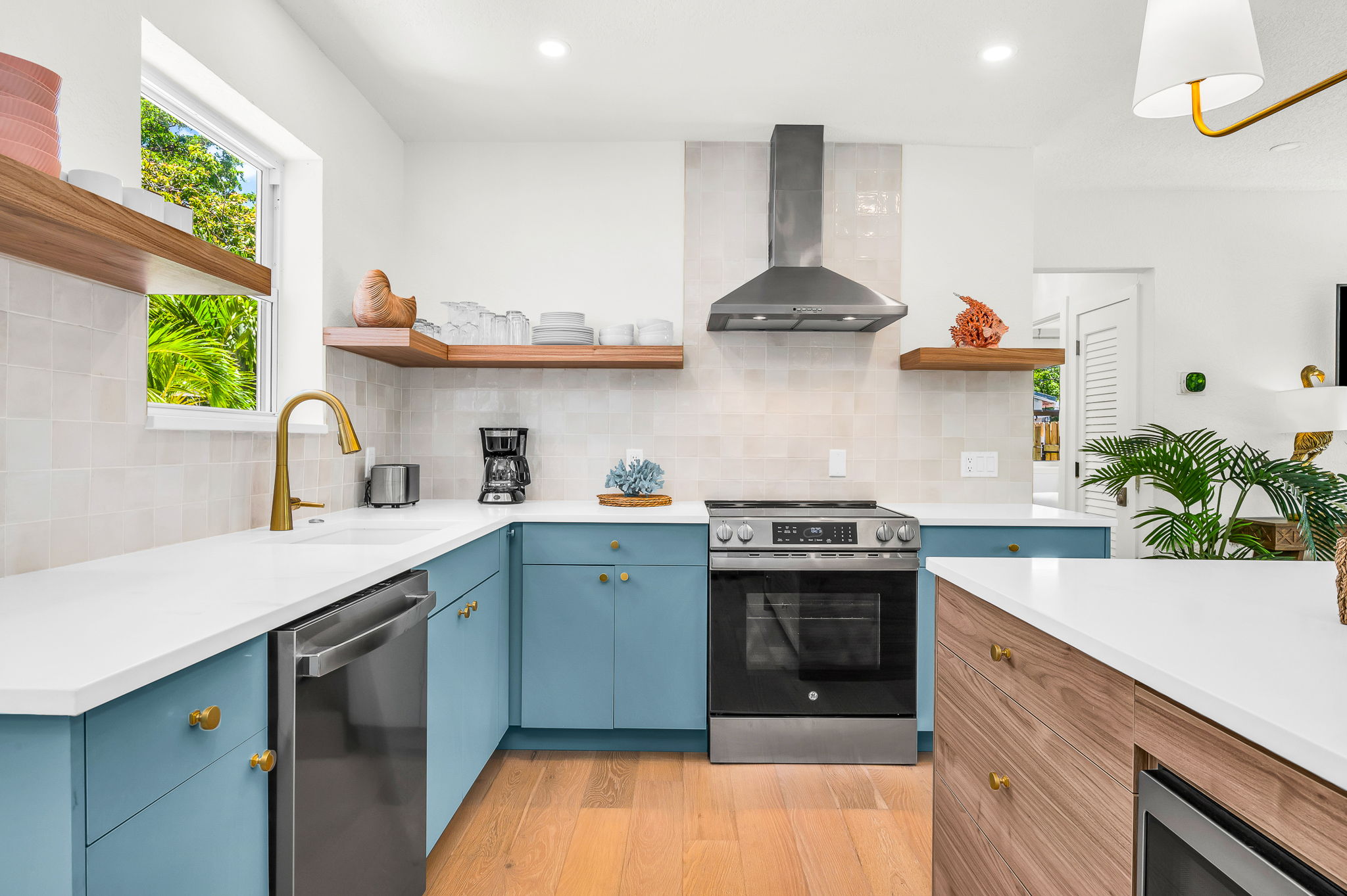 Gourmet kitchen with sleek quartz countertops, custom blue cabinetry, brass accents, and high-end stainless steel appliances. Features an oversized island with seating, open shelving, and designer lighting—perfect for both cooking and entertaining in style