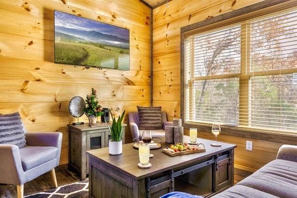 Snuggle up in the inviting living room with your favorite beverage. Soft chairs, warm wood walls, and natural light streaming through the large window create the perfect space to relax and enjoy quiet moments with loved ones.
