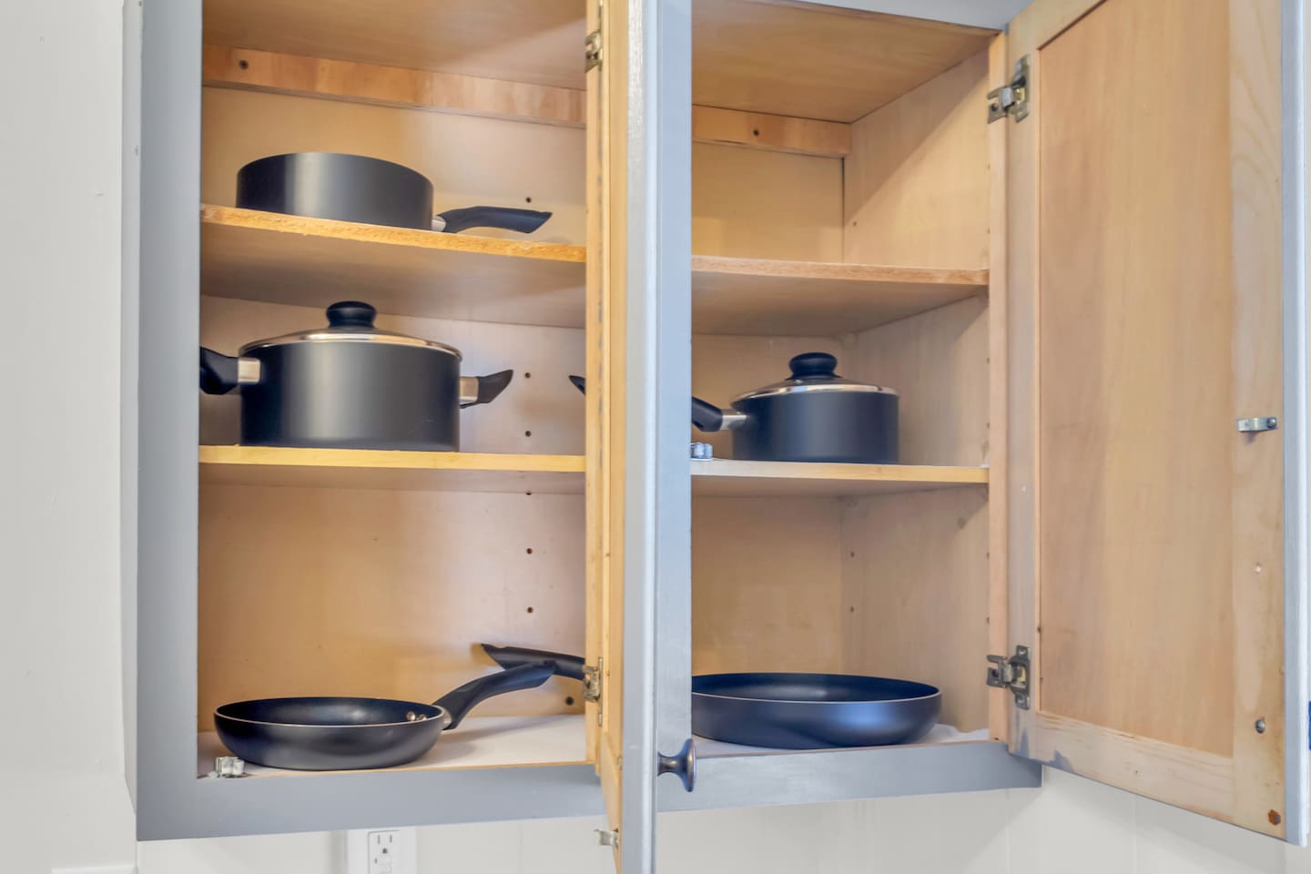 Kitchen cabinet stocked with cookware and essentials.