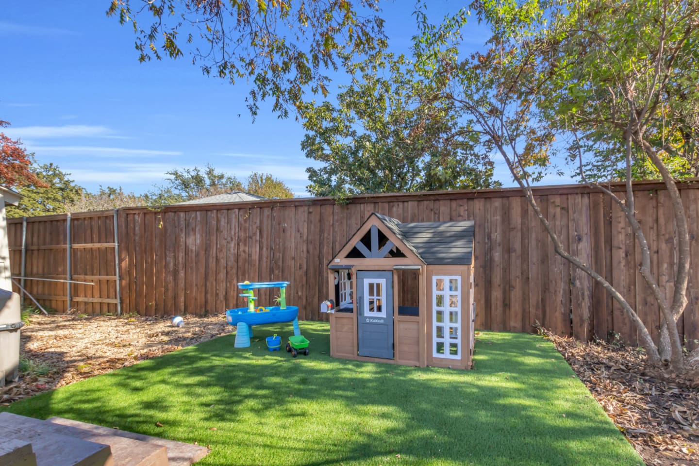 Spacious kid-friendly yard with a dedicated play zone, featuring a mini cottage, water table, and soft turf—perfect for families traveling with young children.
