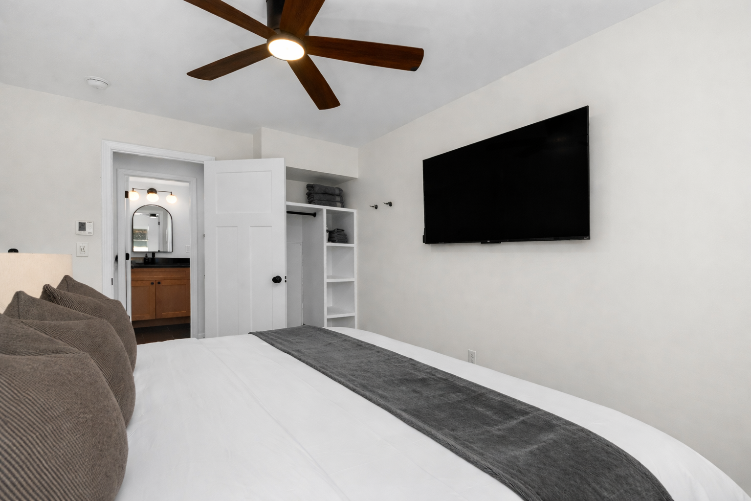 Spacious bedroom with a plush king bed, ceiling fan, smart TV, and easy access to the bathroom—designed for comfort and convenience.