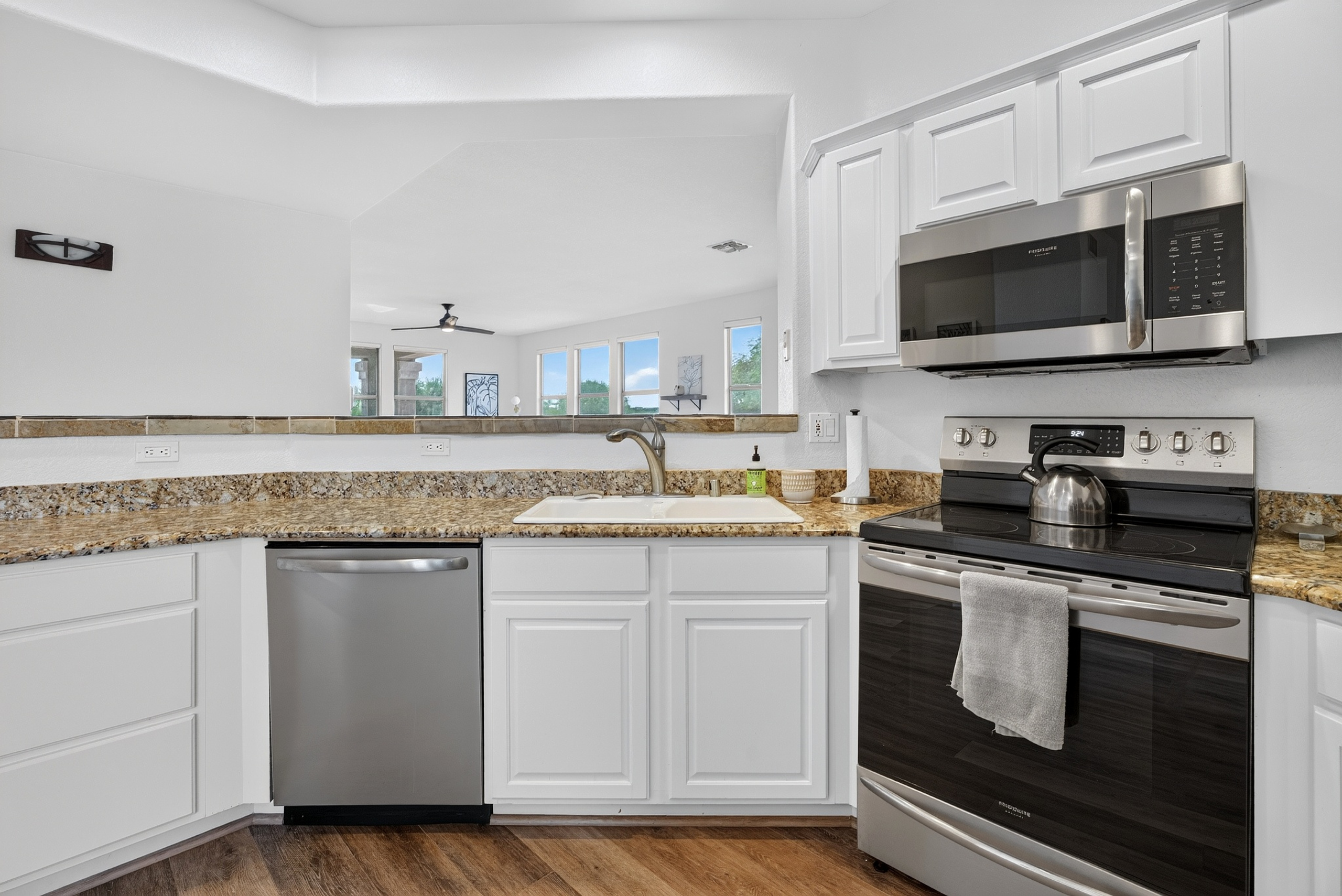 Kitchen with stainless steel appliances, dishwasher, granite counters, and open views into the living area.