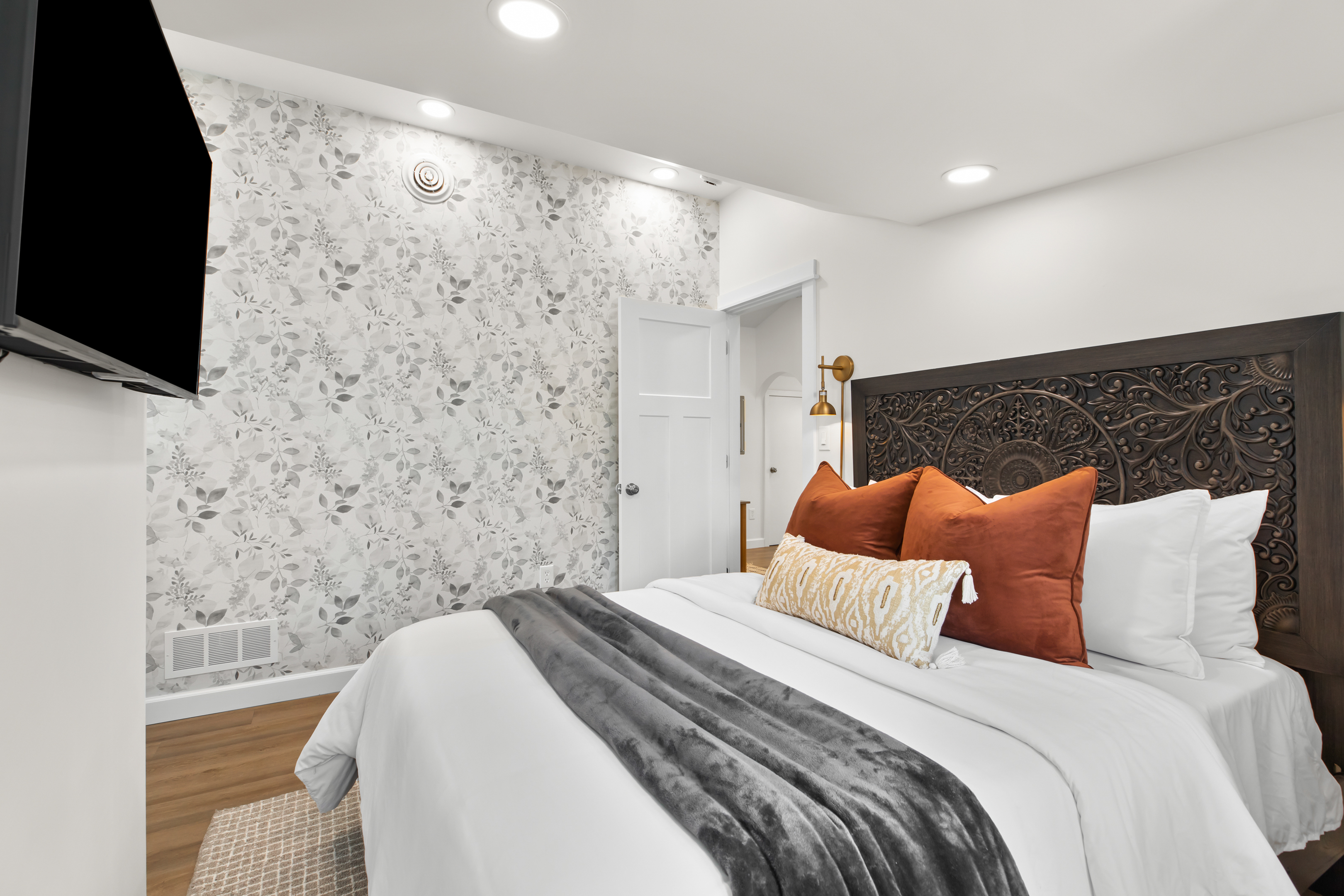 Elegant bedroom featuring bold accent wallpaper, plush bedding, and a wall-mounted smart TV.