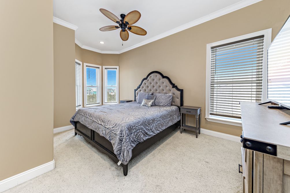 Guest bedroom with upholstered headboard, ceiling fan, and corner windows overlooking the lagoon