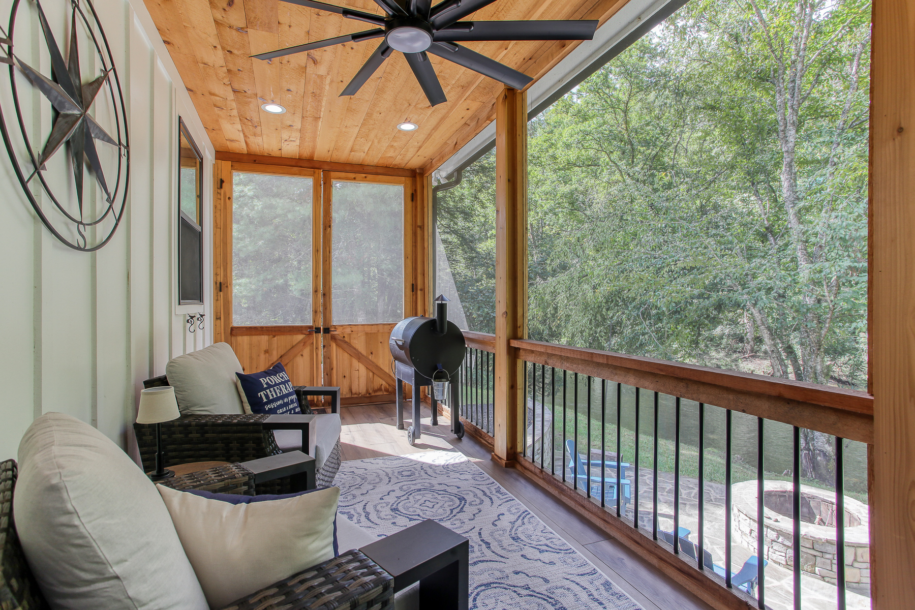 Unwind in the cushioned seating on the screened porch at Robbin’s Nest on Snowbird Creek, with a ceiling fan overhead and trees all around.