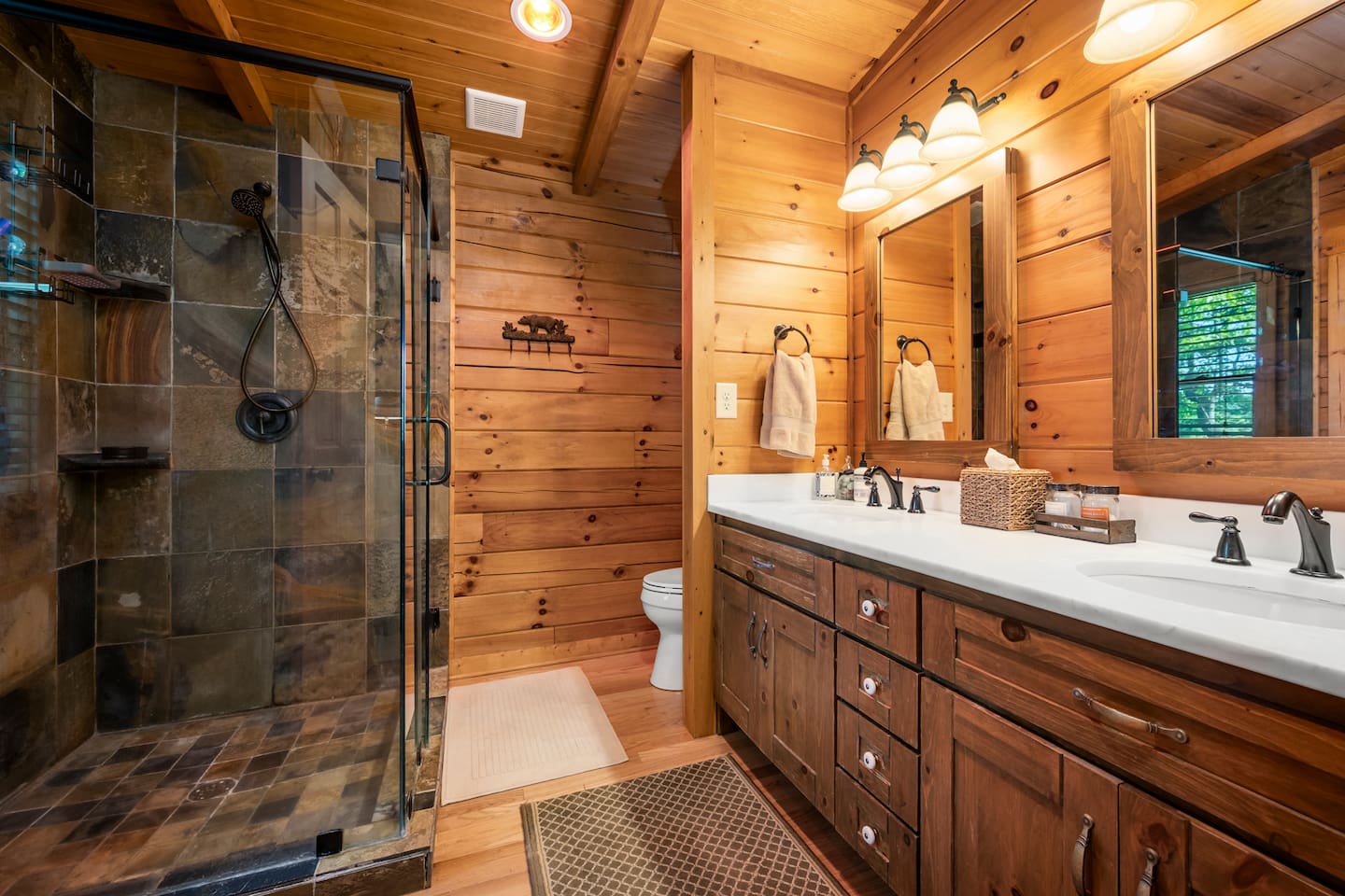 Rustic, full master bathroom featuring a spacious tiled walk-in shower, double vanity, and warm wood finishes throughout