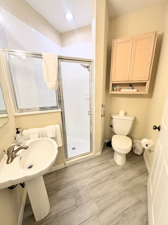 Bathroom with pedestal sink, walk-in shower, toilet, and clean neutral finishes.