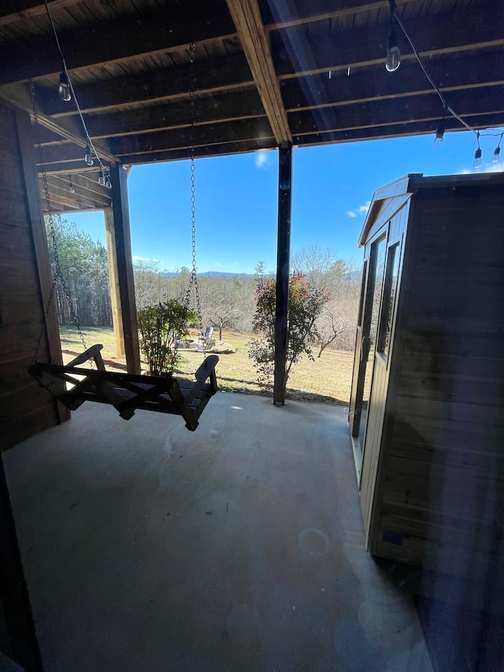 Patio off of the basement bedroom with a bench swing and infrared sauna, and views of the backyard with firepit and orchard trees!