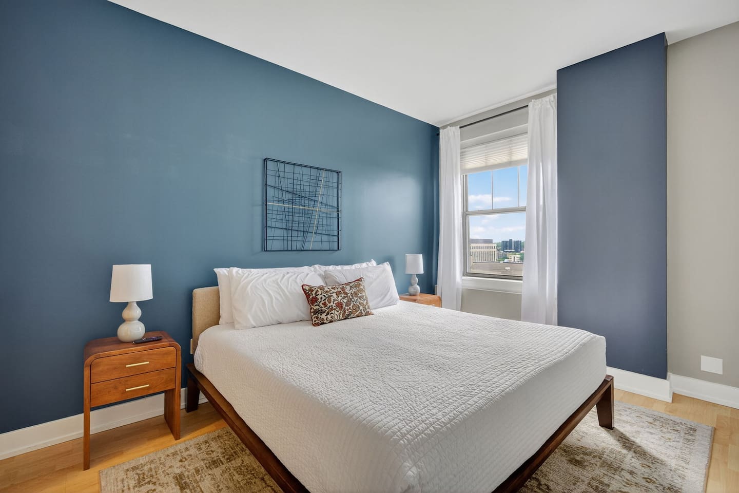 Unwind in a serene bedroom featuring a plush king bed, soft linens, and calming blue accent wall. Wake up to natural light streaming in from city-view windows.  Your private retreat for relaxation in downtown Des Moines.