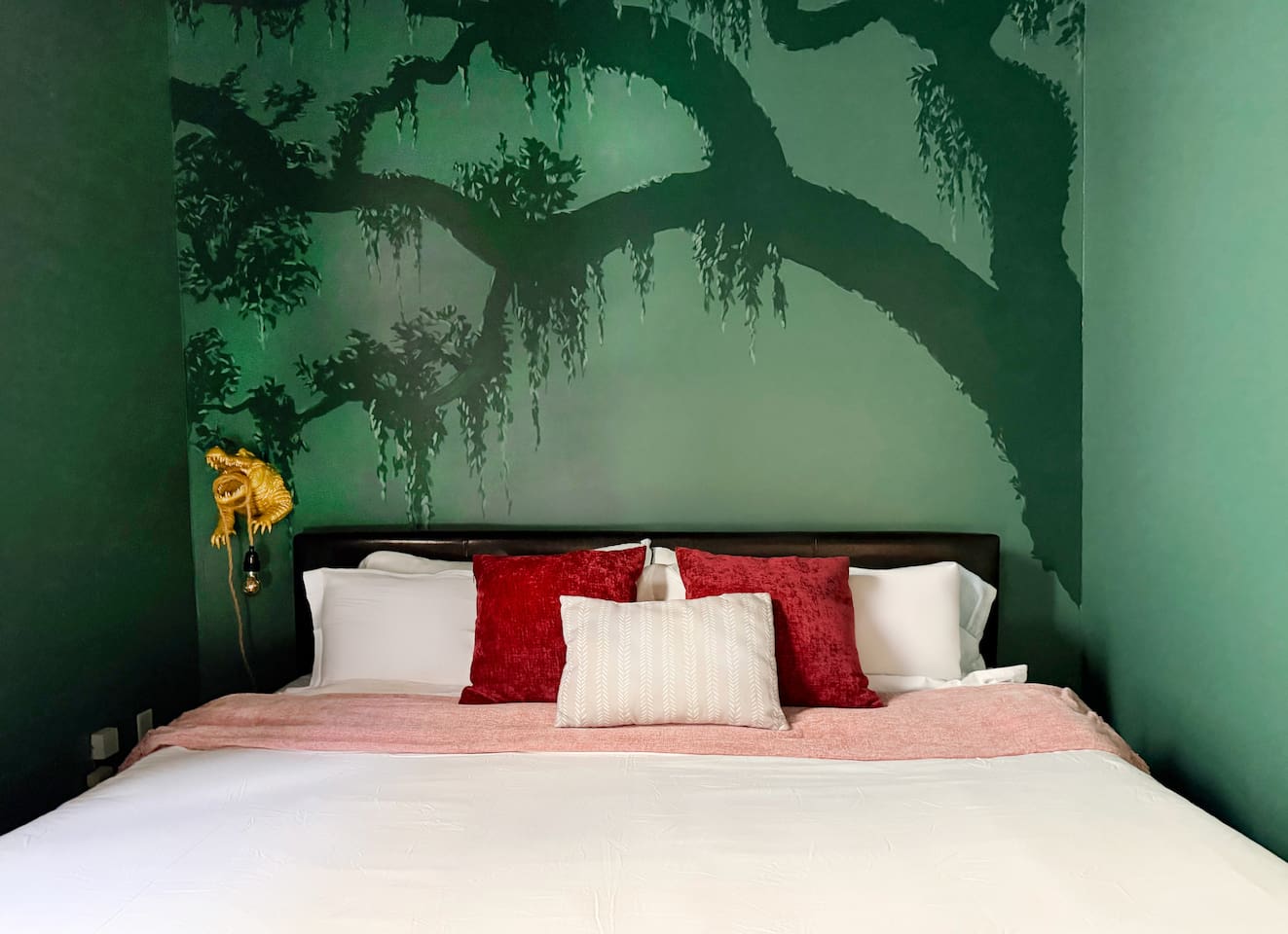 Sleep under the stars without leaving the city. The oak mural wraps around you like the bayou at midnight — moss, mystery, and a golden gator keeping watch from the bedside. Wake up when you're ready. NOLA will still be there.