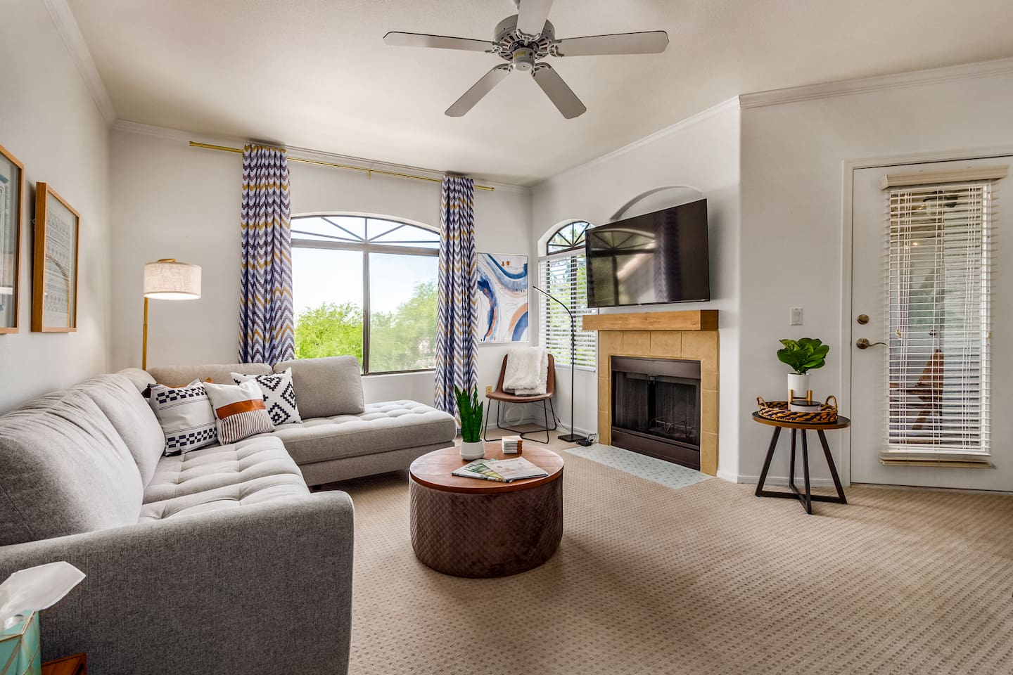 Living room with sectional seating, wall-mounted TV, fireplace, ceiling fan, and natural light from arched windows.
