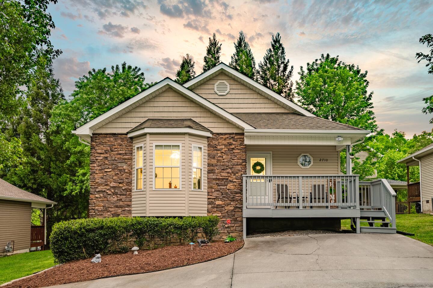 Inviting cottage-style home with stone accents, a welcoming front porch, and lush greenery—perfect for a cozy getaway in a peaceful setting.