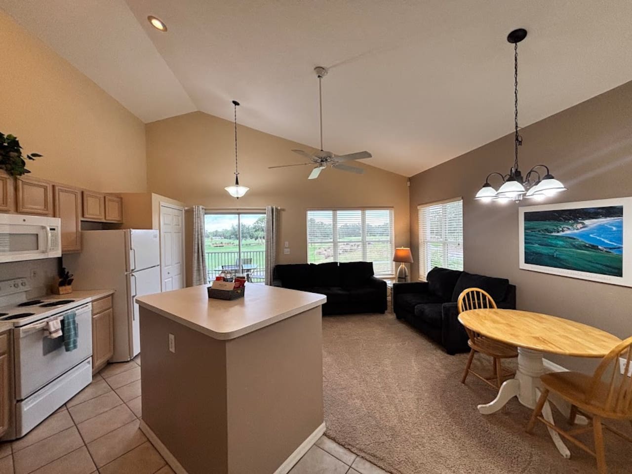 Open-concept kitchen, dining, and living area with vaulted ceilings, comfortable seating, and views out toward the screened balcony.