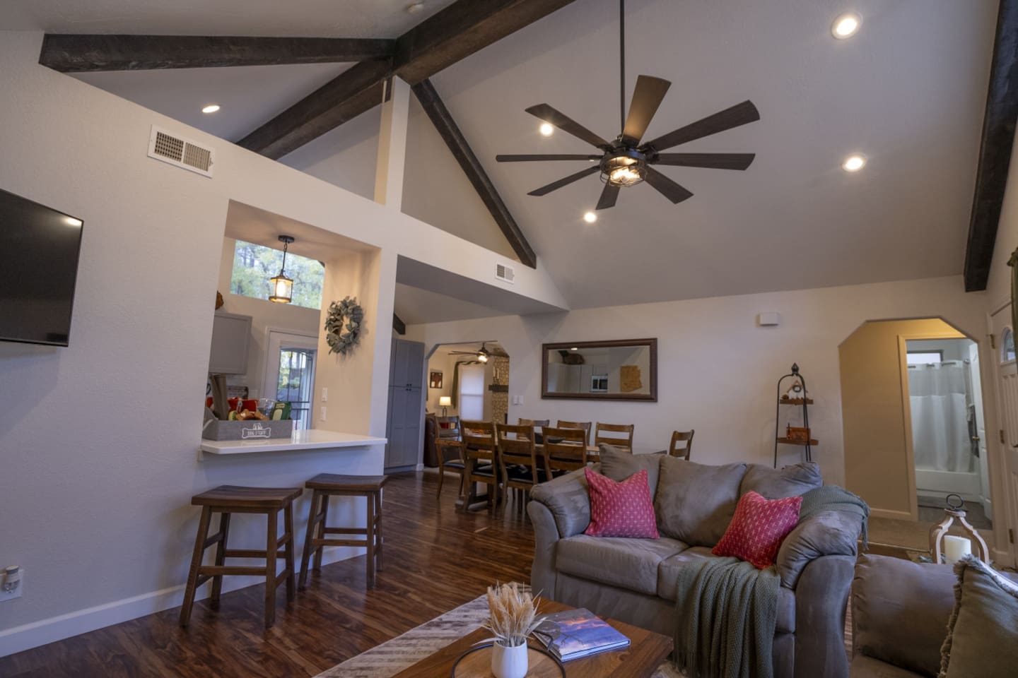 Open living room with vaulted ceilings, exposed beams, bar seating, and easy flow into the dining area.