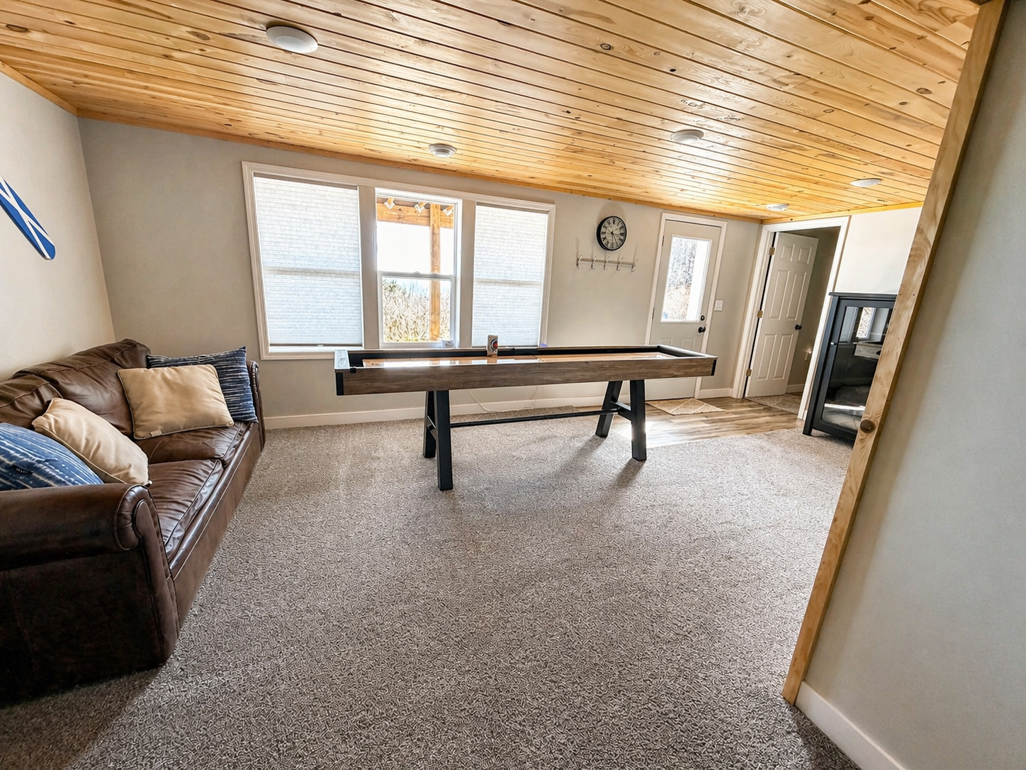 As you head back through the basement, passing the shuffleboard, large windows offer a view of the backyard, guiding you toward the bedroom. The walkout door and natural light make this space feel connected to the outdoors.