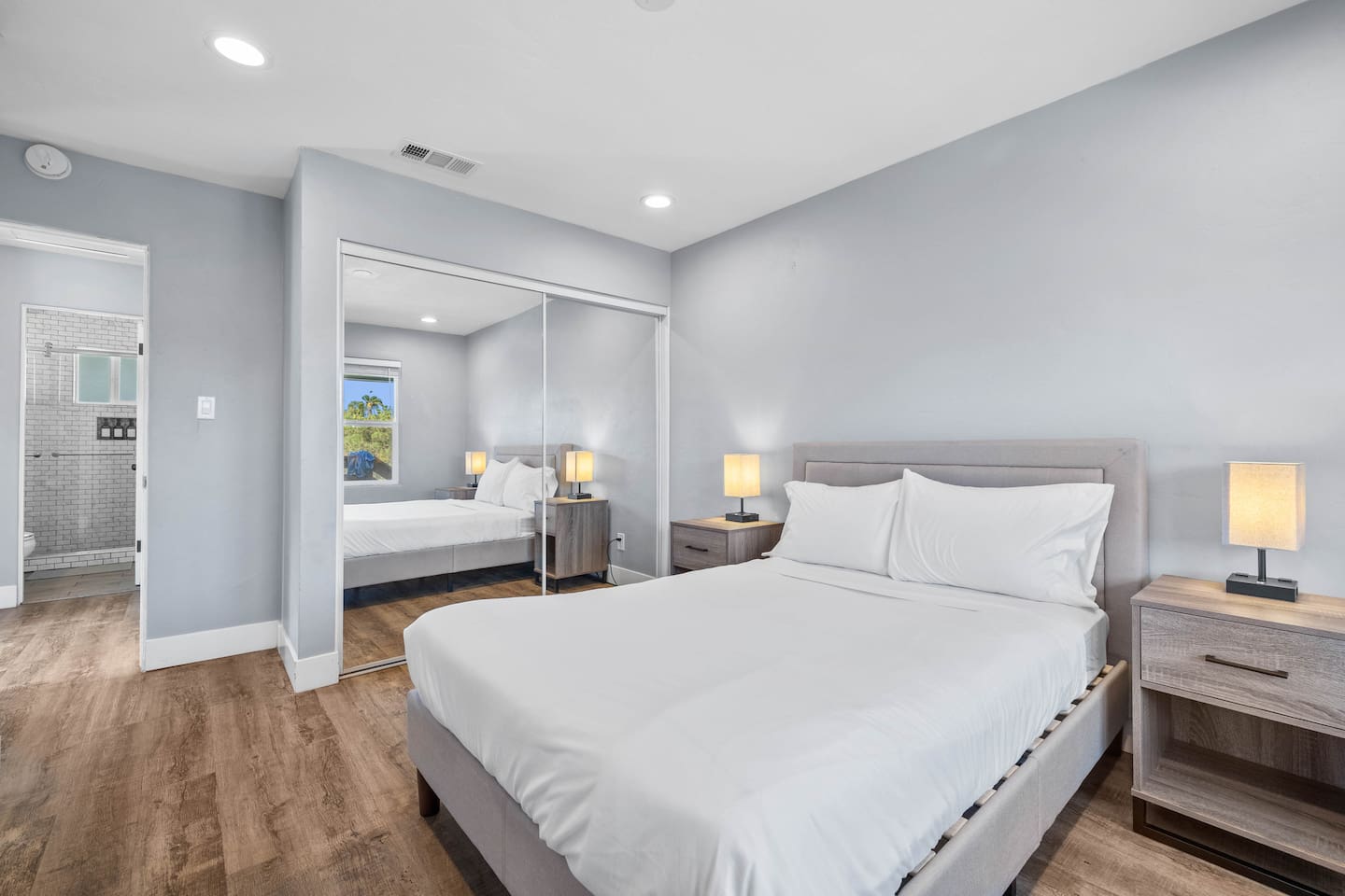 Cozy bedroom featuring a comfortable bed with two lampshades providing aesthetic lighting, a full-body mirror, and a convenient clothing container inside. A perfect blend of style and functionality for a relaxing and organized stay.