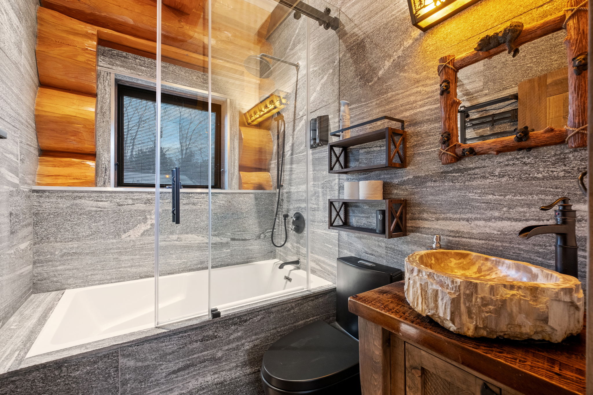 Beautiful full bathroom featuring a deep soaking tub with glass enclosure, natural stone sink, and lodge-style rustic finishes.
