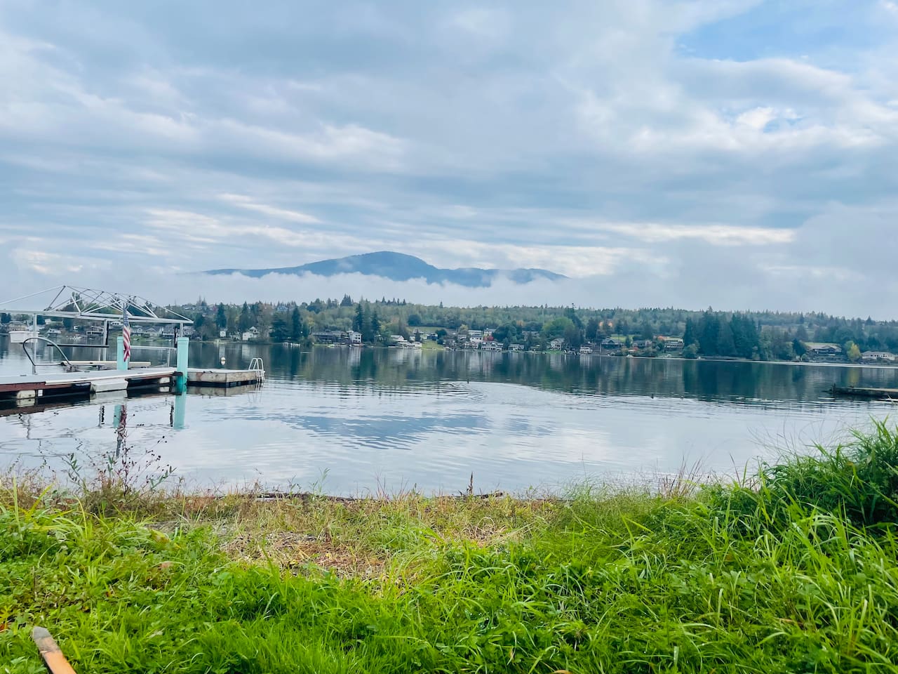 Looking out across the lake, the dock rests to the right along the shoreline. Calm water reflects the sky and surroundings, creating a peaceful, inviting scene of the lakeside setting.