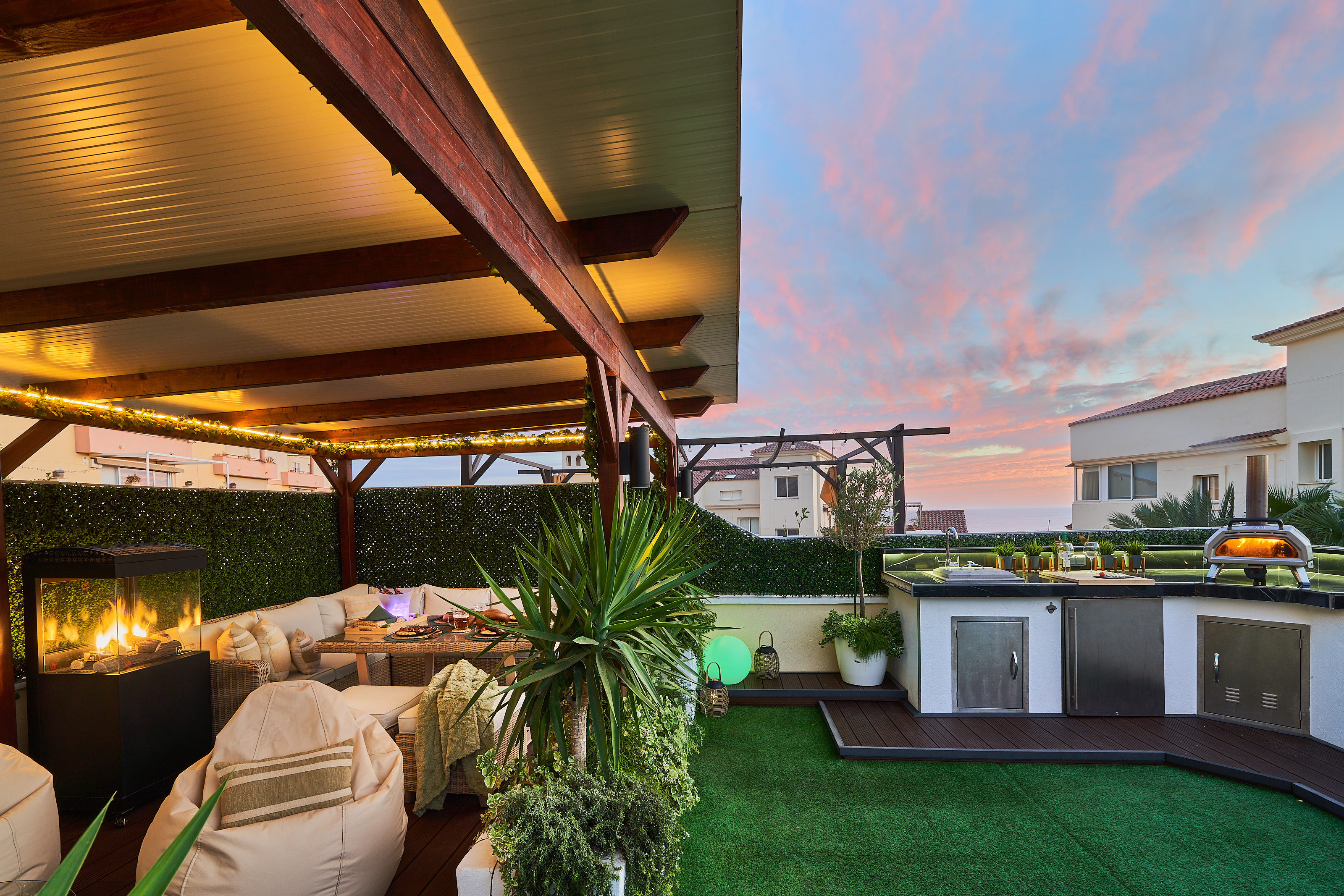 Fire up the built-in barbecue or the wood-fired pizza oven and enjoy cooking with a view. The fully equipped outdoor kitchen features a sink, fridge, and prep space with subtle lighting for evening meals. Dine under the open sky at the outdoor table, surro