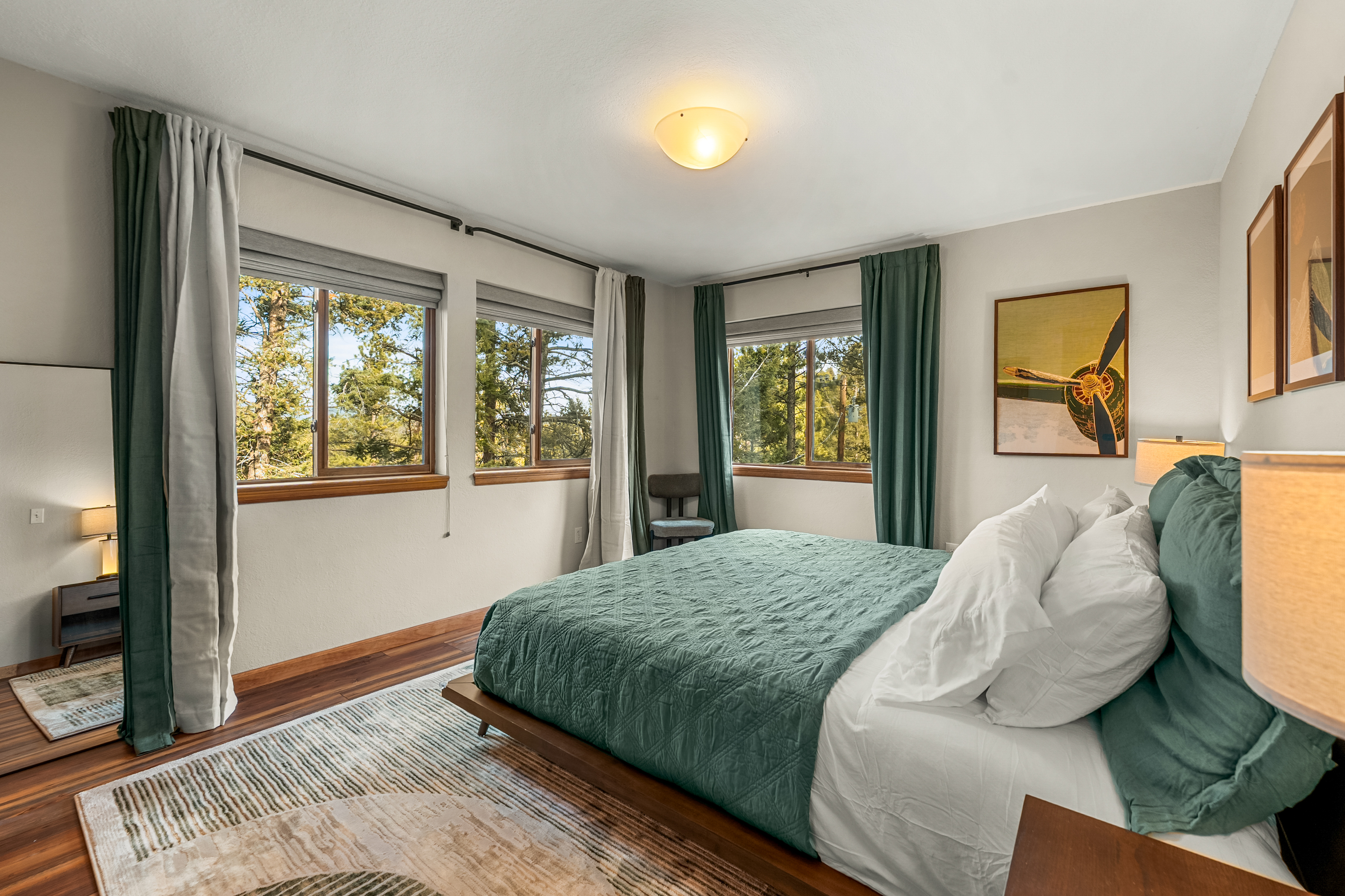 🛏️🌲 Bright, airy main-level bedroom with corner windows, crisp linens, and calming forest views ✨—perfect for slow mornings and restful nights.