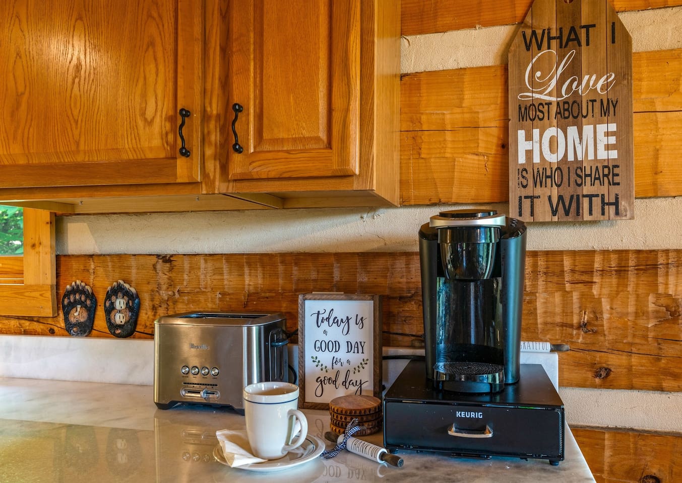 Cozy Kitchen corner with the coffee station. A toaster, Keurig coffee maker, and "Today is a Good Day" sign add to the warm vibe. View of greenery outside.