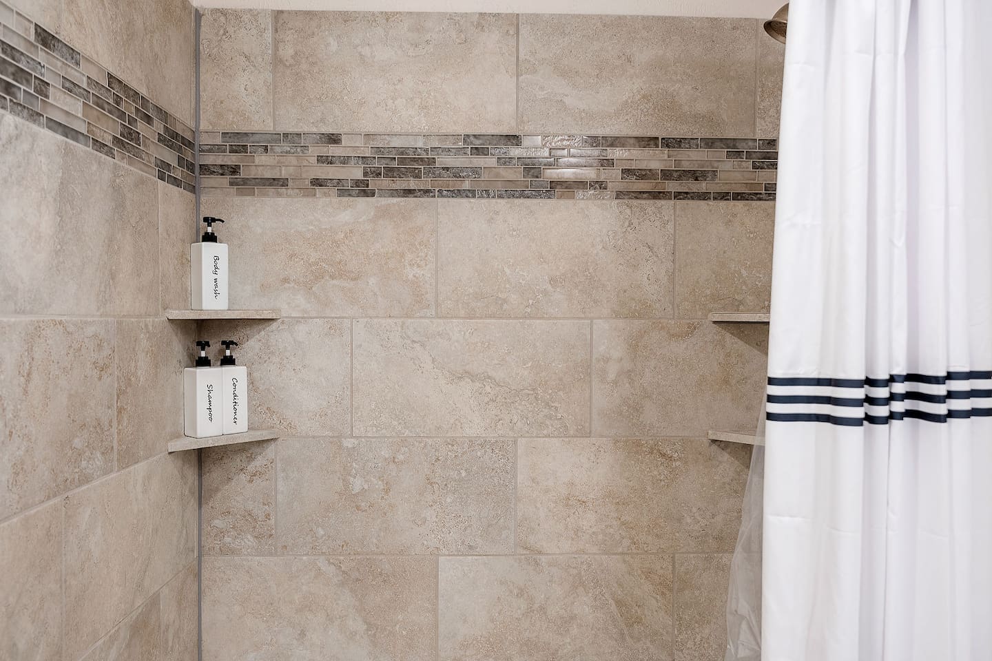 Enjoy a spacious shower area featuring elegant tile work and built-in shelves. The provided toiletries add to the convenience and comfort.