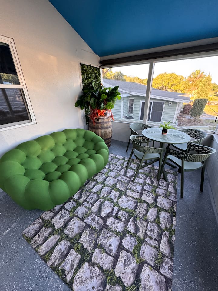 Spacious outdoor patio at Mario's Mini Mansion in Clermont, FL! Oversized green "football" couch, stone paver rugs, and dining table perfect for relaxing or enjoying meals al fresco with the whole family. Bamboo shades can unroll for extra privacy!
