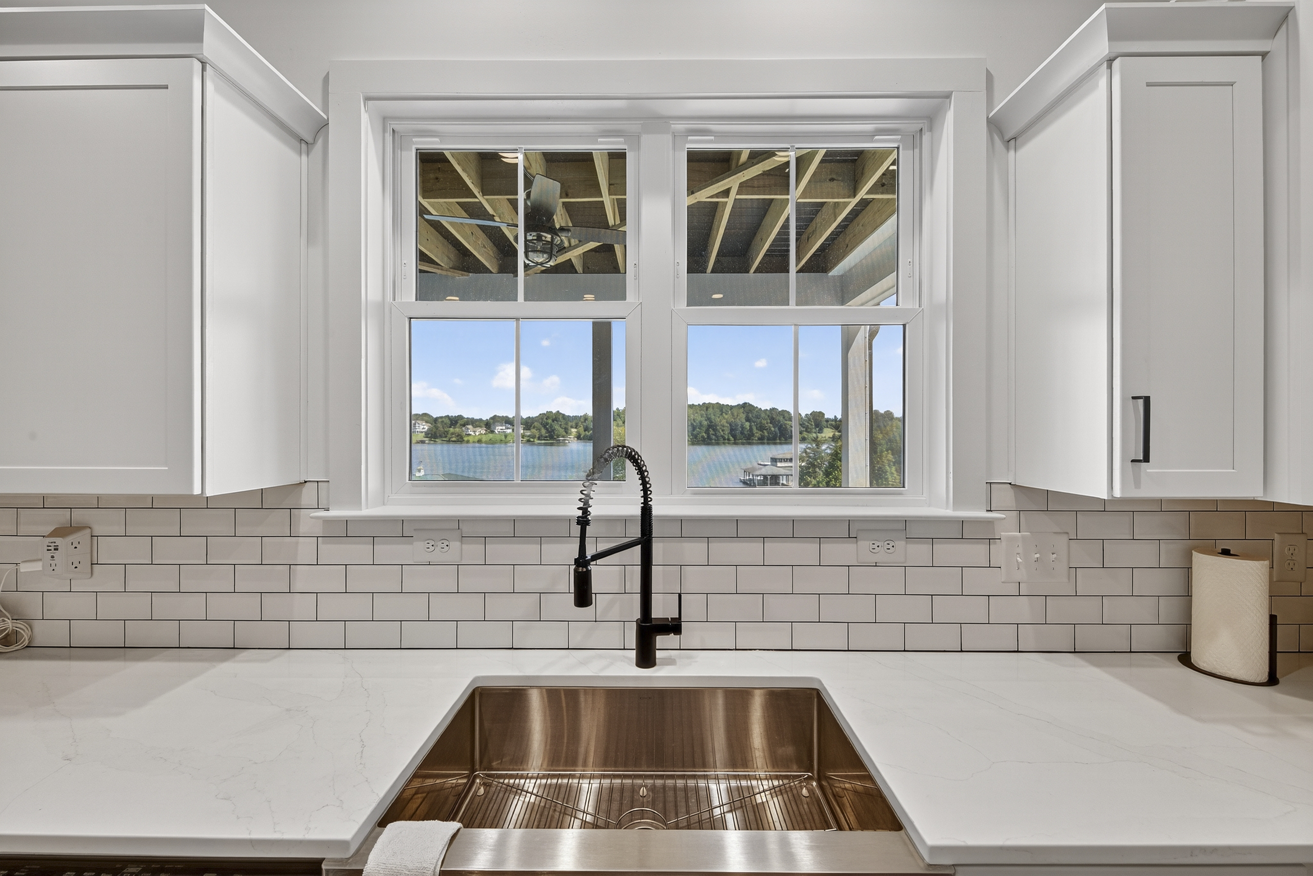 A modern farmhouse sink sits below large windows that overlook the covered deck and lakefront yard.